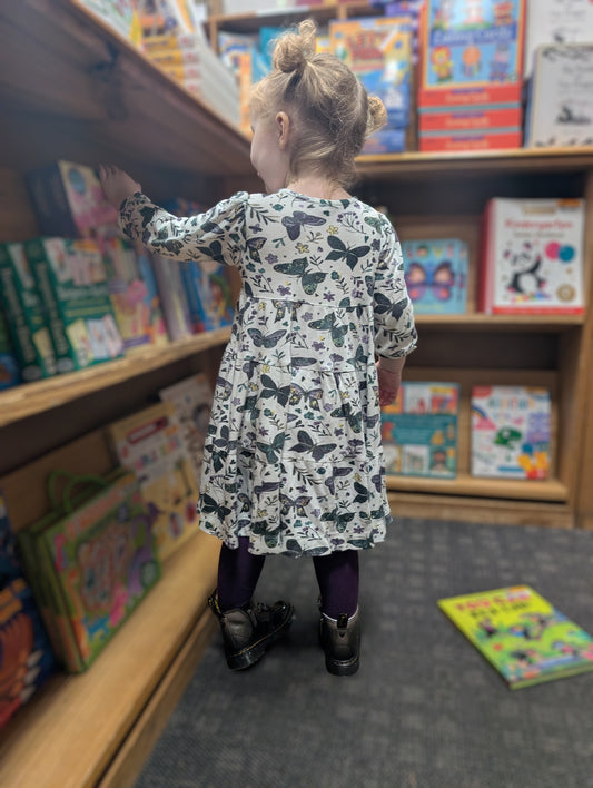 Child in Anne dress in dark butterflies standing in front of a bookshelf filled with books.