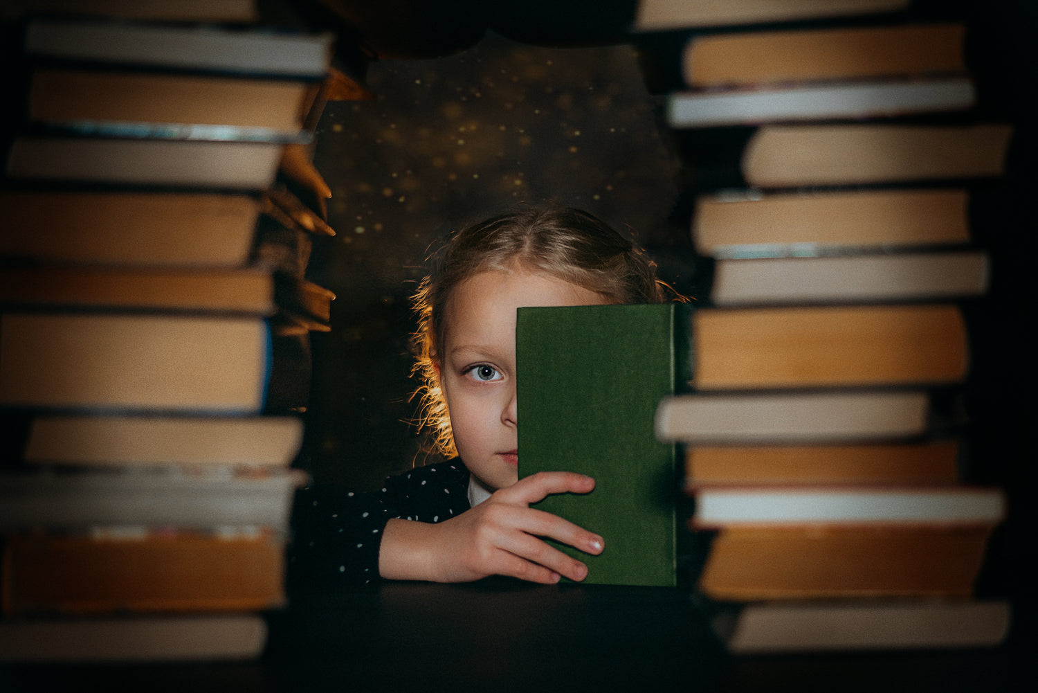 Child holding a book in front of a stack of books with a dark background