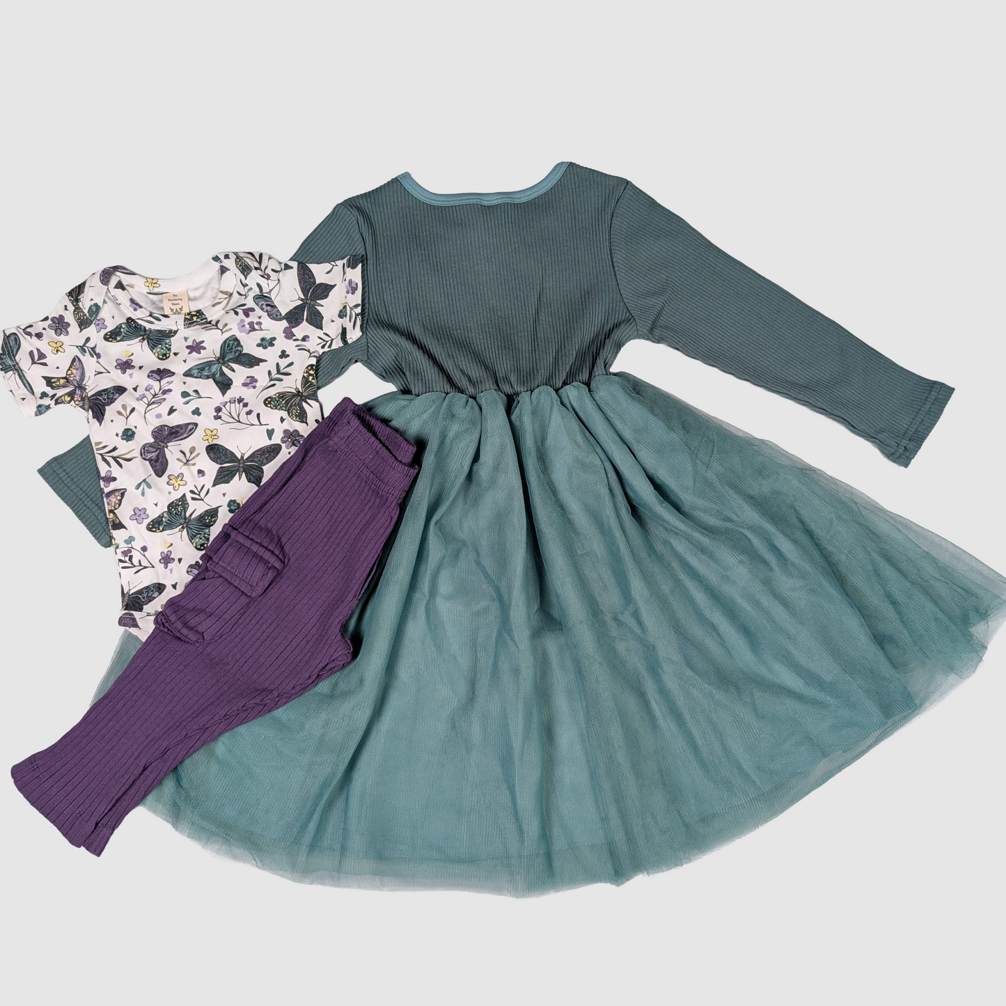 Teal dress with long sleeves, purple leggings, and a butterfly-patterned shirt on a light gray background