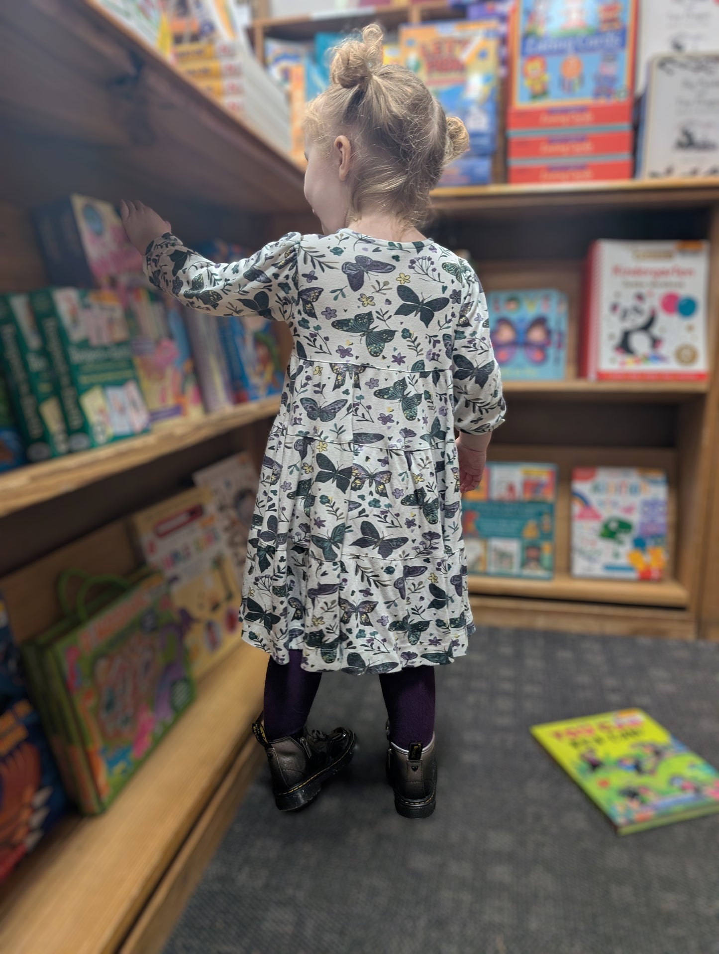 Child in Anne dress in dark butterflies standing in front of a bookshelf filled with books.