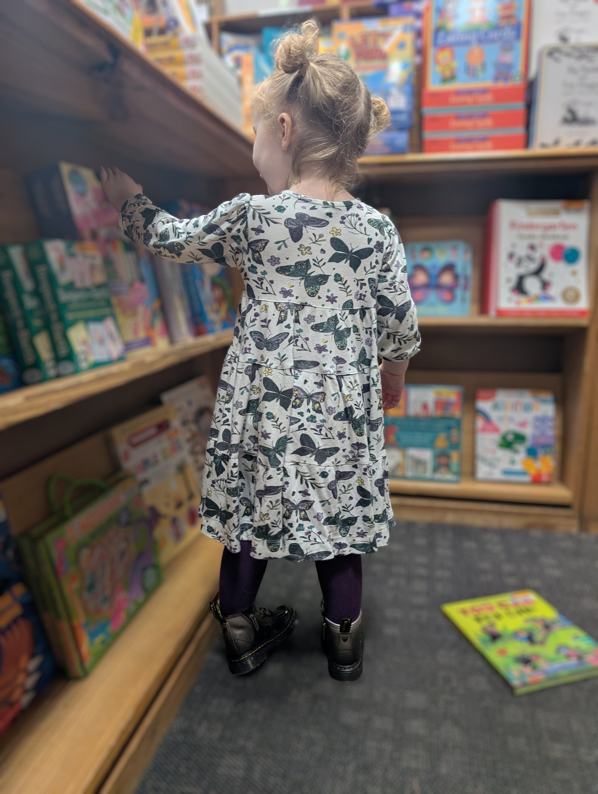 Child in Anne dress in dark butterflies standing in front of a bookshelf filled with books.