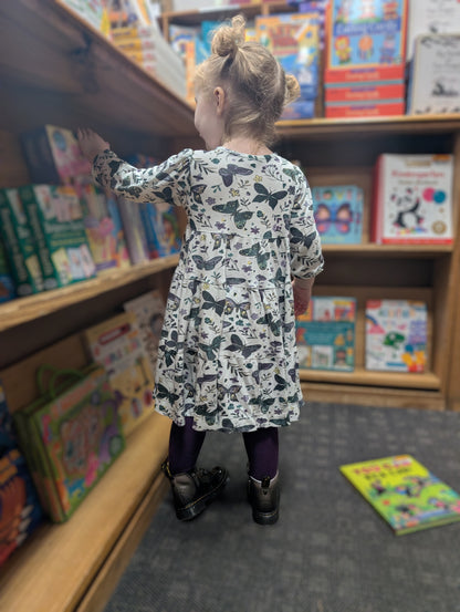 Child in Anne dress in dark butterflies standing in front of a bookshelf filled with books.