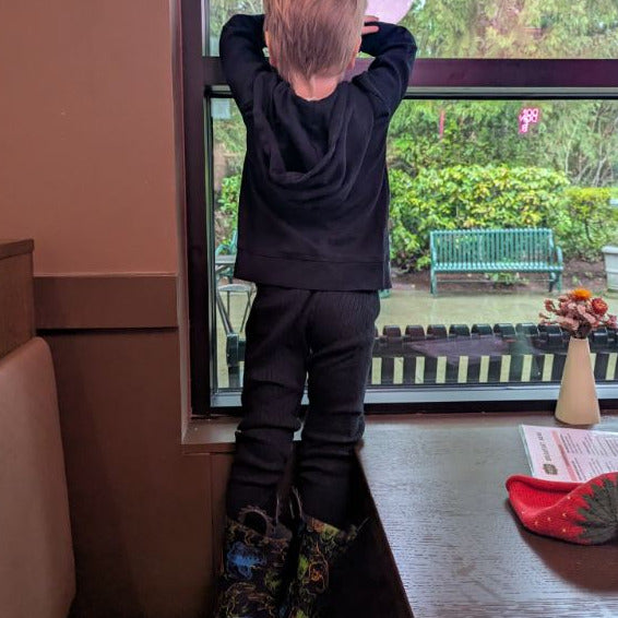 Child in a black outfit standing by a window looking outside